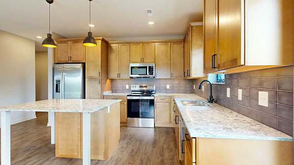 A kitchen with warm wooden cabinets, quartz countertops, a central island, and stainless steel appliances.
