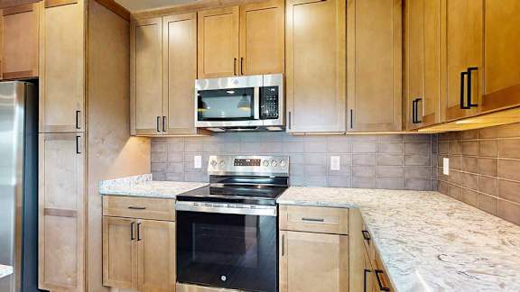 A close up of the stainless steel microwave and range in a kitchen with warm wooden cabinets.