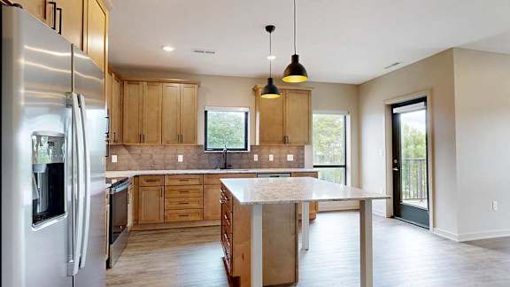 A kitchen with warm wooden cabinets, quartz countertops, a central island, and stainless steel appliances.