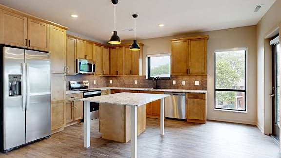 A kitchen with warm wooden cabinets, quartz countertops, a central island, and stainless steel appliances.
