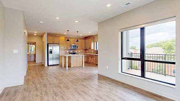 An open-concept kitchen with warm wooden cabinets and a large central island, that flows into a spacious living room with oversized windows.