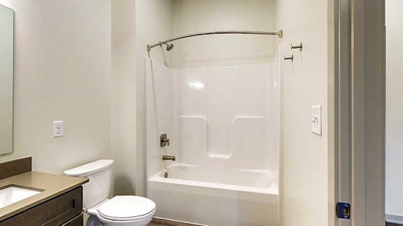 a bathroom with a white shower tub, and the edge of a vanity sink with quartz countertop