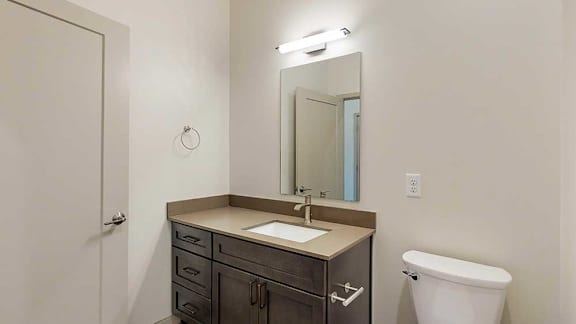 a bathroom with a quartz vanity sink, mirror, and overhead over lighting