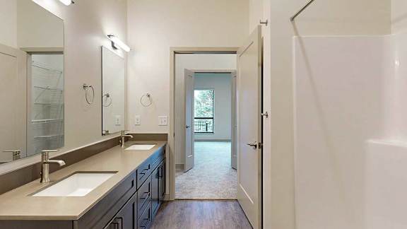 a bathroom with a double sink, mirror, and a door leading to a walk-through closet