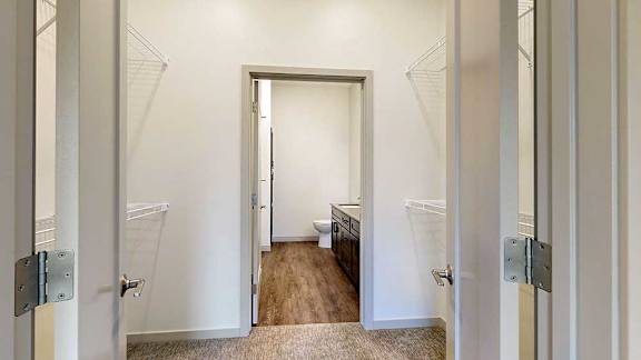 a closet with built-in shelving and hanging space that connects the primary bedroom to the primary bathroom