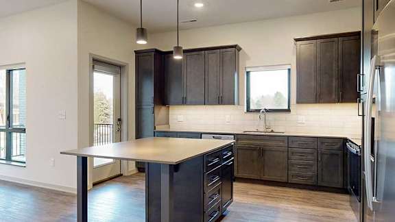 a kitchen with dark wood cabinets, a large kitchen island table, stainless steel appliances, and light quarts countertops