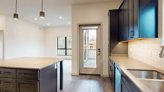 a kitchen with dark cabinets, quartz counter tops, tile backsplash, and a door to the walk-out patio