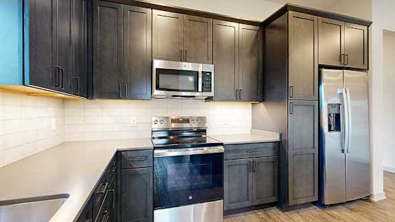 a kitchen with dark wooden cabinets, stainless steel appliances, tile backsplash, and quartz countertops