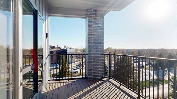 A balcony with a metal railing, a brick pillar and a view of the neighborhood.