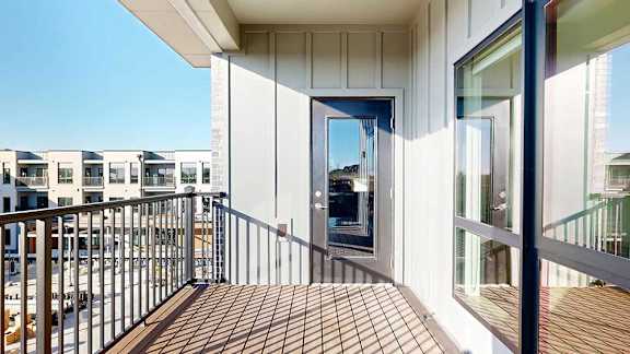 A balcony with a metal railing, a windowed door to the living room, and a view of the courtyard.