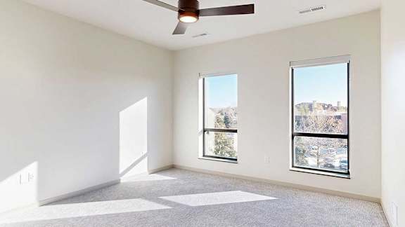 A carpeted bedroom with floor-to-ceiling windows, and a ceiling fan.