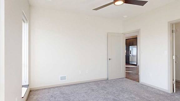 A carpeted bedroom with a walk-in closet, a ceiling fan, and floor-to-ceiling windows.