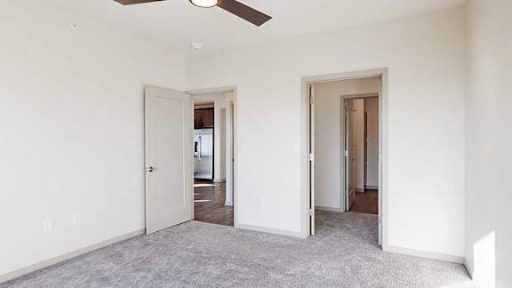 A carpeted bedroom with a walk-through closet to an ensuite bathroom, and a door open to the living room.