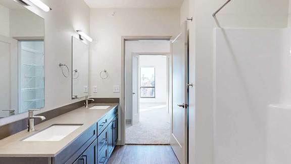 An ensuite bathroom with a quartz double sink vanity, walk-in shower, and a door open to a walk-through closet.