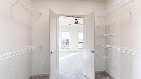 A walk-through closet with wire shelving on either side, and a door open to a bedroom.