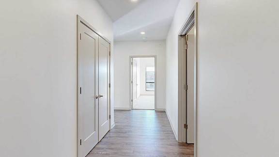 A hallway with a closet to the side, and an open door to a bedroom at the end.