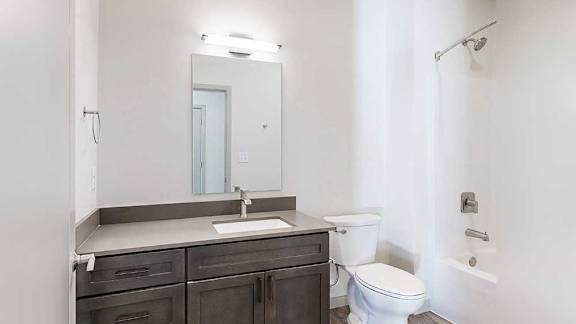 A bathroom with a wide quartz vanity, dark wooden cabinets, and a tub shower with brushed nickel fixtures.