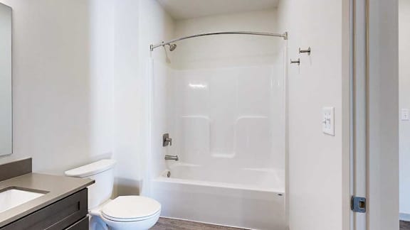 A bathroom with a white tub shower with brushed nickel fixtures, and a curved shower curtain rod.