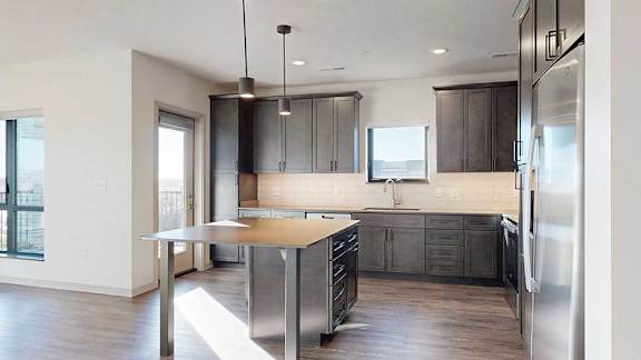 A kitchen with dark wooden cabinets, quartz countertops, a table island, and stainless steel appliances.