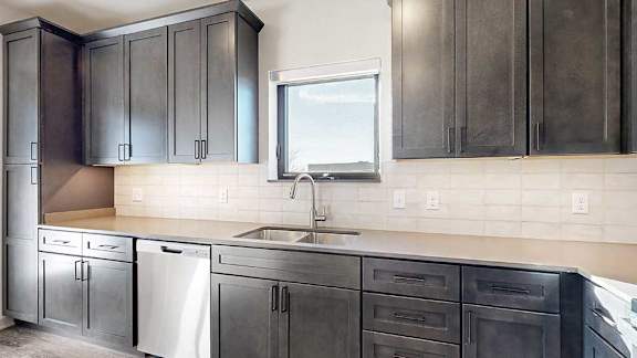 A kitchen with dark wooden cabinets, quartz countertops, a tile backsplash, and a window over the kitchen sink.