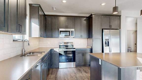 A kitchen with dark wooden cabinets, quartz countertops, a table island, and stainless steel appliances.