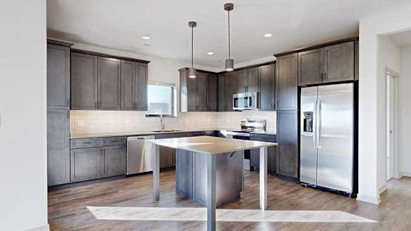 A kitchen with dark wooden cabinets, quartz countertops, a table island, and stainless steel appliances.