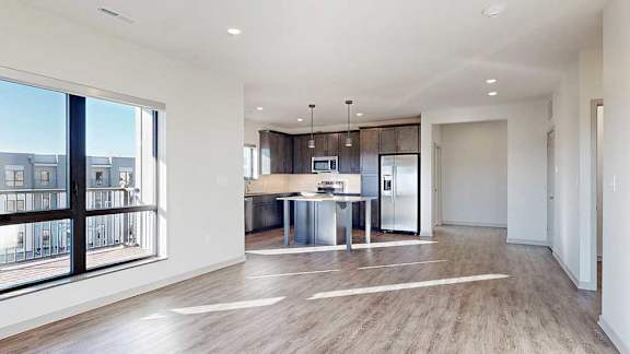 A living room with hardwood-style flooring and kitchen with dark wooden cabinets.