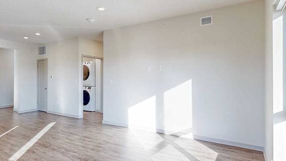 A living room with hardwood-style flooring, with a hallway to a laundry room.