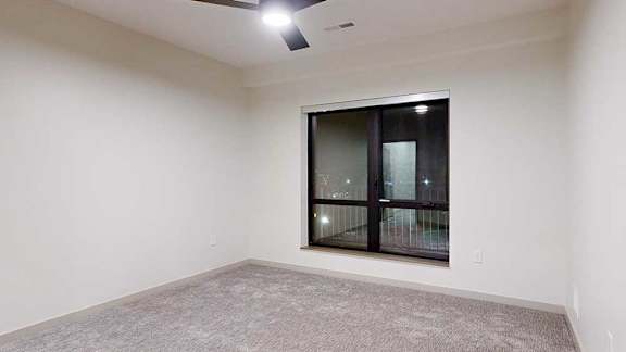 a bedroom with a large window, carpeted flooring, and a ceiling fan