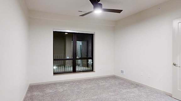 a bedroom with white walls, a large window, a ceiling fan, and carpeted flooring