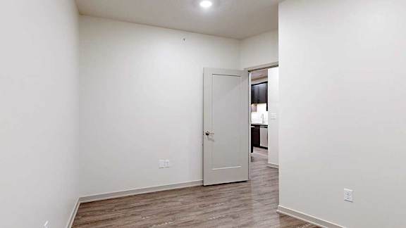 a den with hardwood flooring and a door to the kitchen area