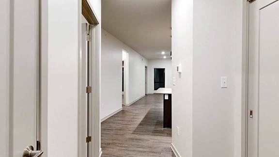a hallway with closed closets on either side leading to an open kitchen and living room area