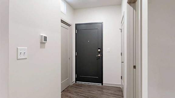 a dark grey front door in a hallway next to closed closets