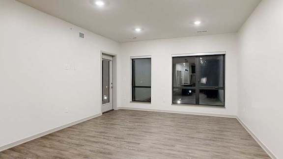 a living room with two large windows, a windowed door to the balcony, and hardwood flooring