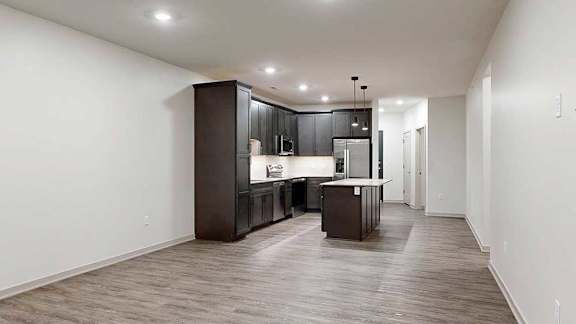 an open living room and modern kitchen featuring dark wood cabinets and a large central island