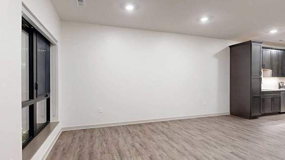 a living room with a wide wall and a large window next to a kitchen with dark wooden cabinets