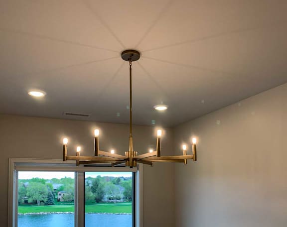 a chandelier with eight candle-style lights hangs from the ceiling in a room with a view of a pond and trees outside the window