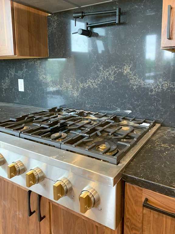a stainless steel gas stove with six burners, a pot-filler faucet, and a marble backsplash