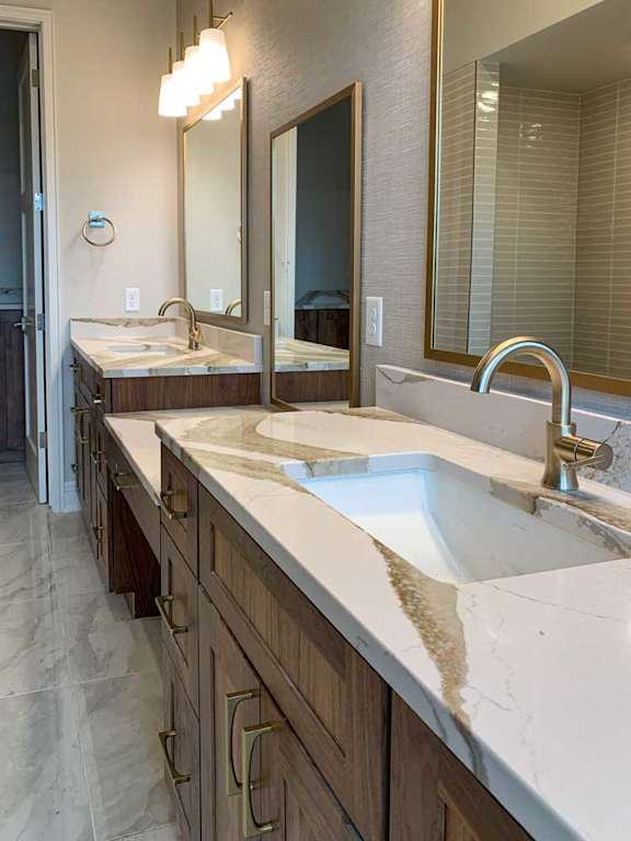 a bathroom with two marble vanity sinks and three tall mirrors