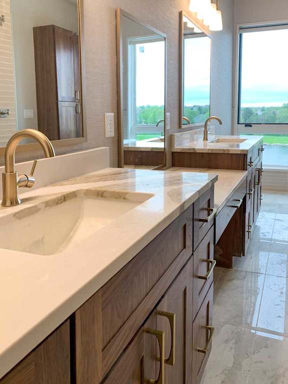 a bathroom with two marble vanity sinks and three tall mirrors, and a large window at the end