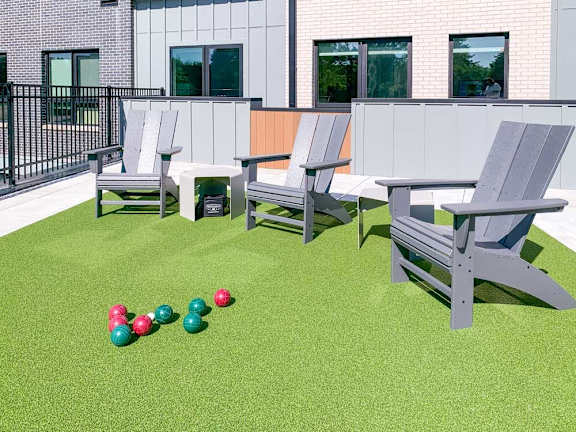 a set of bocce balls in front of Adirondack chairs on a green turf