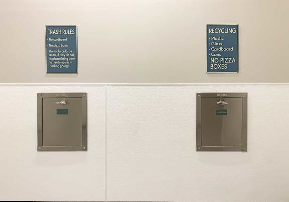 Two stainless steel wall chutes - one for trash and the other for recycling, we respective signs designating what goes into each.
