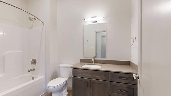 Apartment bathroom with a single-sink vanity, bathtub and shower, and bright lighting.