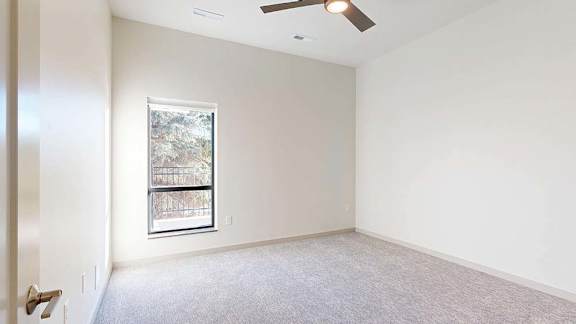 Bright, empty apartment bedroom with neutral carpet, white walls, a vaulted ceiling, and a large window providing natural light.