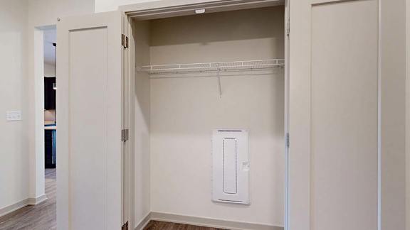 Apartment laundry closet with bifold doors, upper wire shelf, washer and dryer hookups, and hard-surface flooring at the entry.