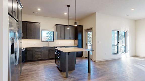 Open apartment kitchen with dark cabinets, island, stainless steel appliances, and wood-style flooring.