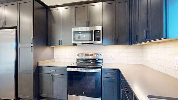 Apartment kitchen with dark cabinets, stainless steel oven and microwave, and light backsplash.
