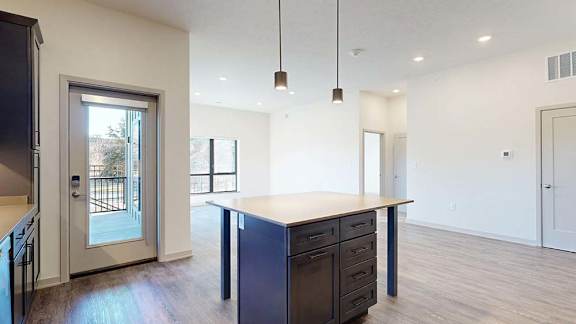Open apartment living area with kitchen island, pendant lighting, wood-style flooring, and patio door.