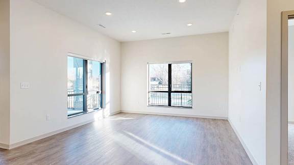 Open apartment living area with wood-style flooring, large windows, and natural light.