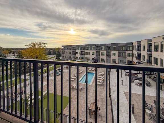 A sunset view from a balcony overlooking a pool and apartment buildings.